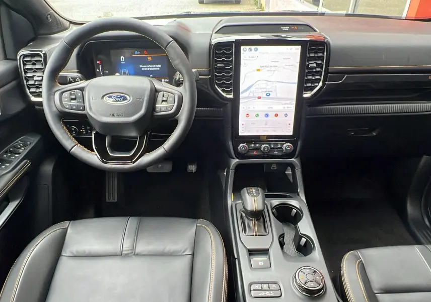 Vue intérieure avant du Ford Ranger Wildtrak Plus 2025, volant cuir, écran tactile vertical et sellerie noire avec surpiqûres jaunes.