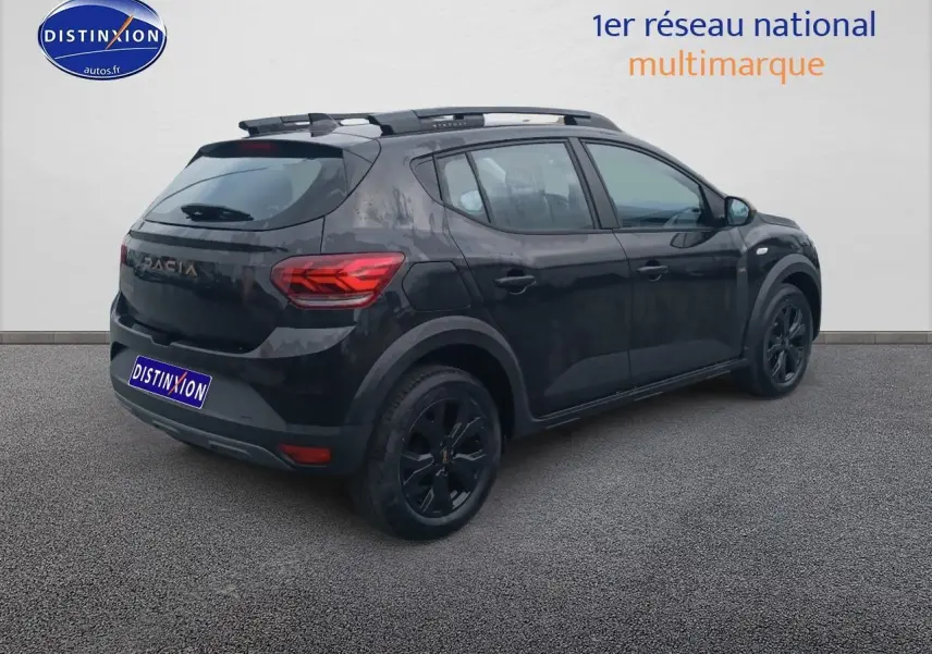 Vue 3/4 arrière droite d'une Dacia Sandero Stepway noire avec barres de toit et jantes alu noires.