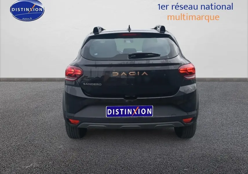 Vue arrière d'une Dacia Sandero noire 2025 avec barres de toit et feux arrière allumés sur fond neutre.