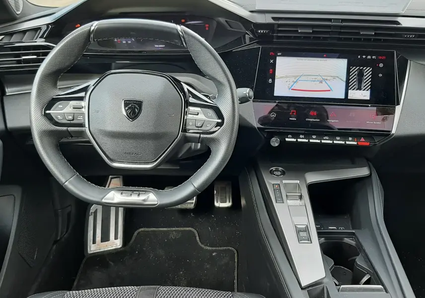Vue intérieure avant de la Peugeot 308 SW 2024, tableau de bord noir avec volant compact GT et écran tactile central.