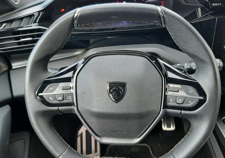 Vue rapprochée du volant cuir noir perforé de la Peugeot 308 SW GT 2024 avec logo et badge GT visible.