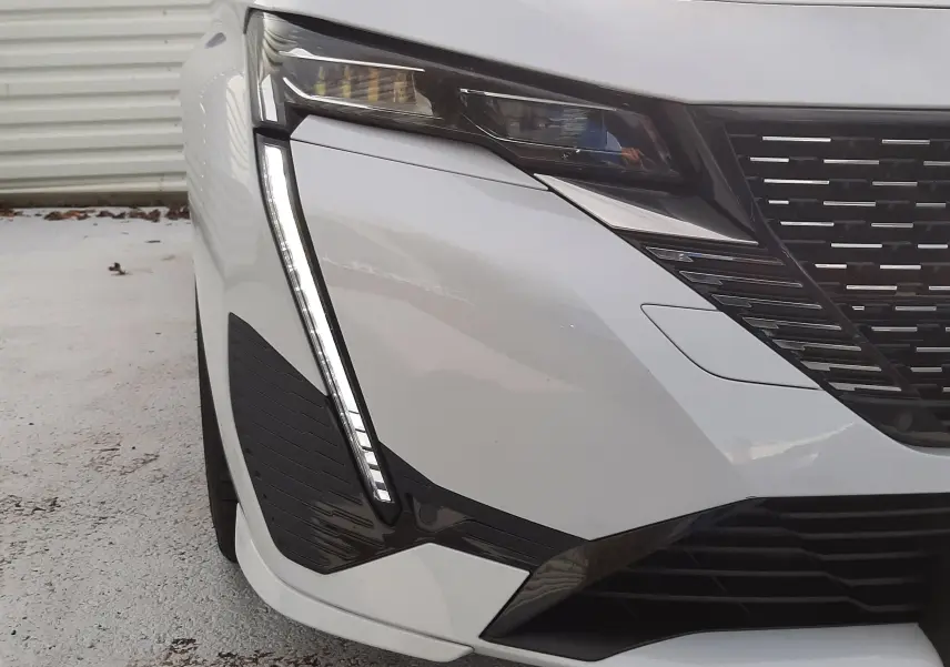 Gros plan sur l'avant gauche blanc Okenite du Peugeot 308 SW 2024, mettant en valeur le phare LED et la calandre noire.