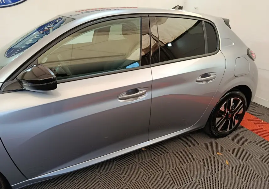 Profil côté gauche d'une Peugeot 208 gris clair 2025 avec jantes noires et rétroviseur noir brillant.