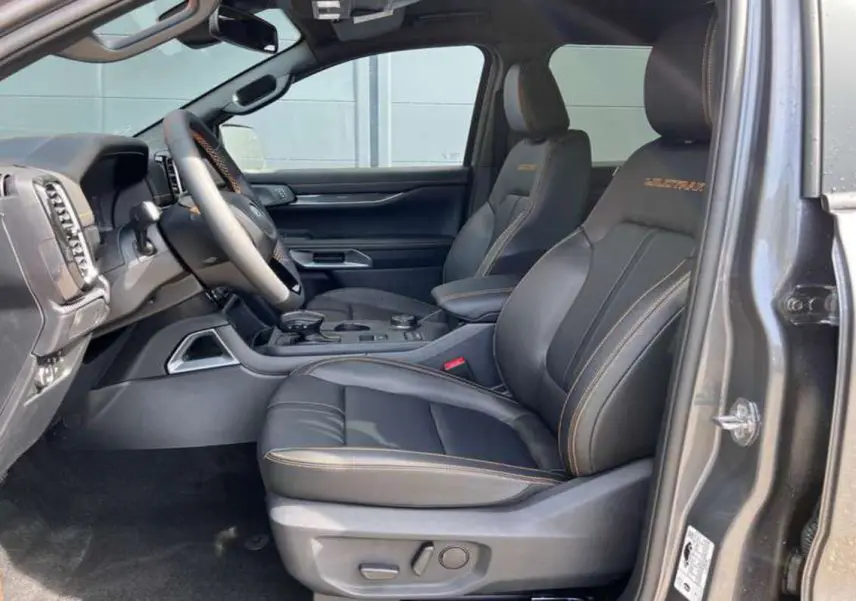 Vue intérieure côté conducteur du Ford Ranger Wildtrak Plus 2025, sièges cuir noirs avec surpiqûres orange et logo brodé.