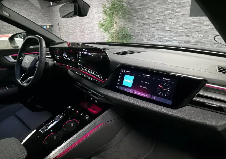 Intérieur Audi A5 Avant 2025 vu côté conducteur, tableau de bord noir avec éclairage d'ambiance rose et double écran tactile.