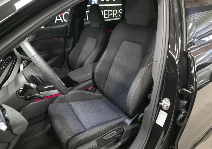 Vue intérieure côté conducteur de l'Audi A5 Avant noire 2025, sièges sport S en tissu avec surpiqûres beige cardamome.