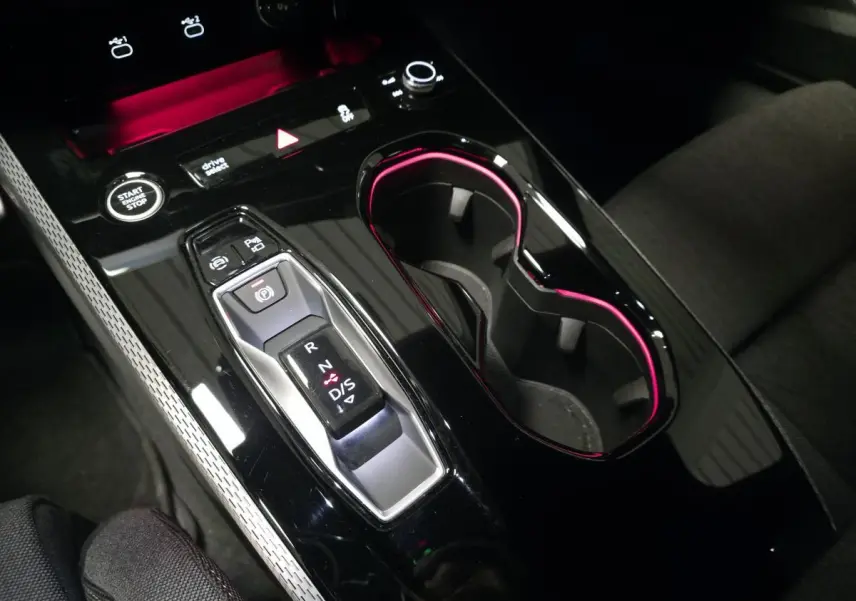 Gros plan sur la console centrale noire brillante de l'Audi A5 Avant 2025 avec éclairage d'ambiance rose autour des porte-gobelets.