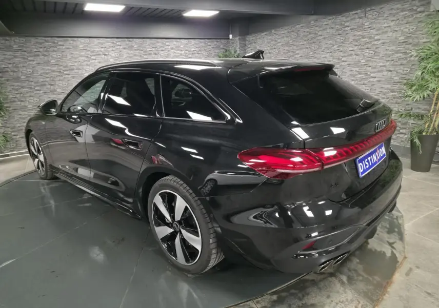 Audi A5 Avant noir vue 3/4 arrière droit en intérieur avec jantes 19 pouces et feux arrière LED continus.