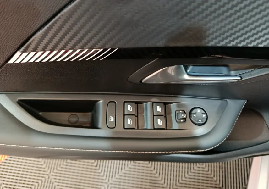 Gros plan sur la commande des vitres et rétroviseurs côté gauche de la porte intérieure noire de la Peugeot 208 gris clair 2025.