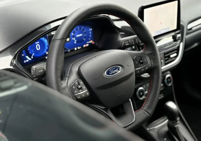Vue intérieure rapprochée du volant ST-Line et du tableau de bord numérique bleu du Ford Puma 2024.