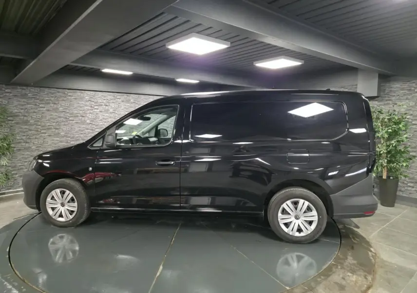 Vue de profil côté gauche d'un Volkswagen Caddy Cargo noir avec jantes acier et portes tôlées en intérieur showroom.
