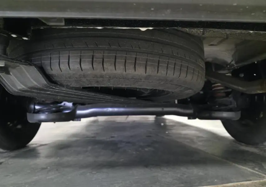 Vue rapprochée sous un Volkswagen Caddy noir 2024 montrant la roue de secours et la suspension arrière.