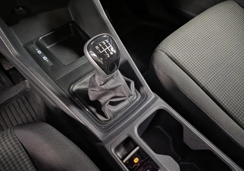 Vue rapprochée de la console centrale du Volkswagen Caddy 2024 noire, avec levier de vitesses manuel et frein à main électrique.