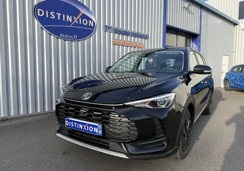 MG Motor ZS Hybrid 197 noir en 3/4 avant droit, avec calandre imposante et phares effilés, stationné devant un bâtiment.