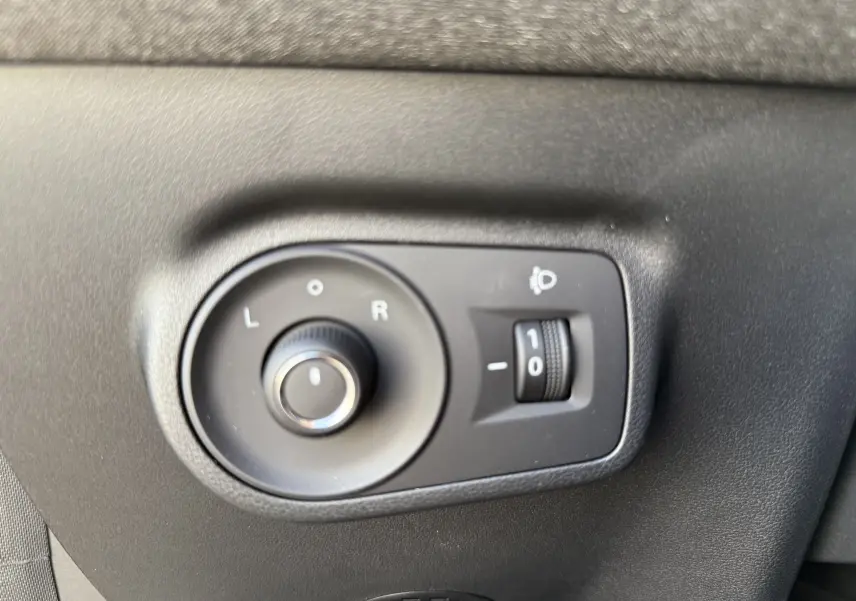 Gros plan sur les commandes noires de réglage des rétroviseurs et des phares intérieures du MG MOTOR ZS Hybrid 2026.