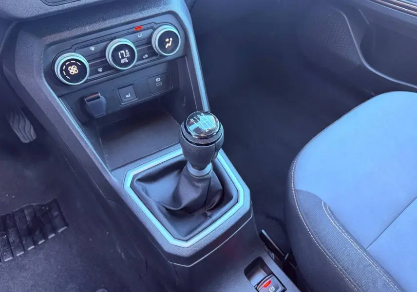 Gros plan sur la console centrale et levier de vitesses manuel, siège avant droit en tissu bleu visible, intérieur DACIA Sandero 2025.