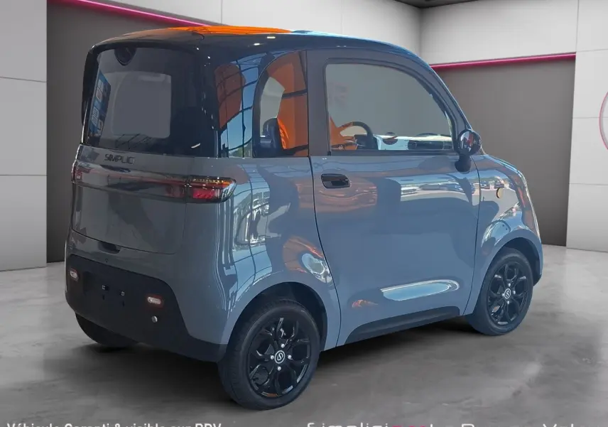 Vue 3/4 arrière droite d'une Simplici S1 électrique gris perle avec toit noir et jantes noires en intérieur showroom.