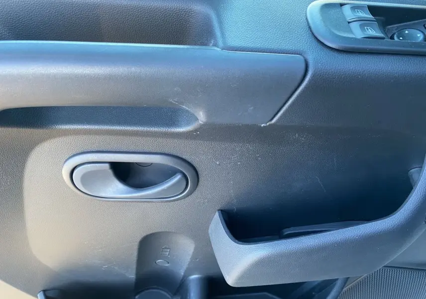 Gros plan sur la poignée intérieure et les commandes de fenêtre côté gauche d'un Nissan Interstar blanc.