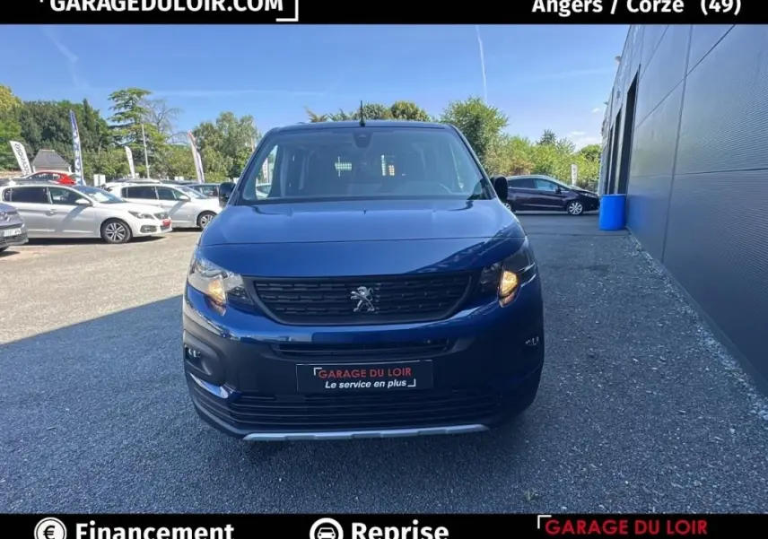 Vue de face du Peugeot Rifter bleu 2024 avec calandre noire et feux avant allumés sur parking extérieur.