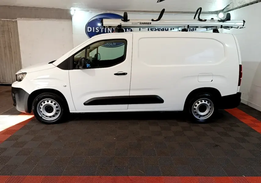 Vue latérale gauche d’un utilitaire Peugeot Partner blanc avec galerie de toit et jantes acier en intérieur fermé.