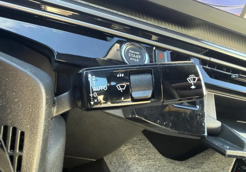 Gros plan sur la commande d’essuie-glace noir brillant et le bouton start/stop du tableau de bord gris du Peugeot 3008 Hybrid 2025.