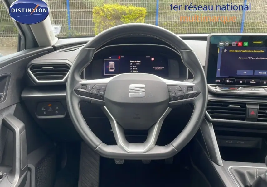 Vue intérieure centrée sur le volant cuir multifonction d'une SEAT Leon blanc neige métal, avec tableau de bord digital et écran tactile.