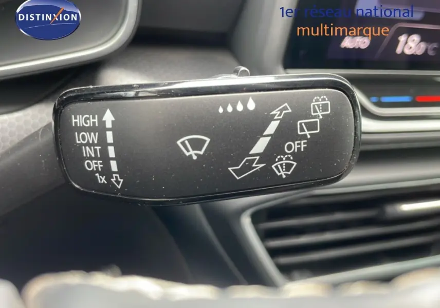 Gros plan sur la commande d’essuie-glace dans l’habitacle du SEAT Leon blanc neige métal, avec tableau de bord en arrière-plan flou.