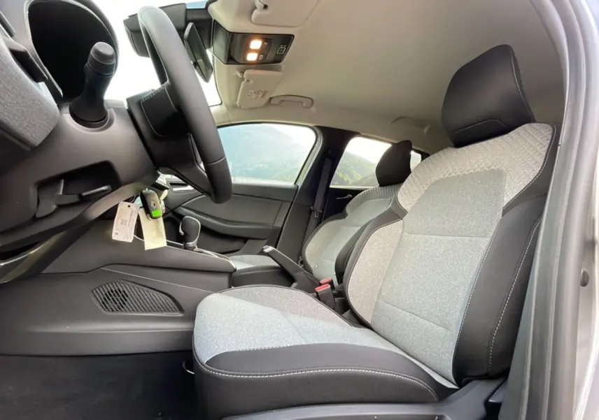 Vue intérieure côté conducteur de la Renault Clio 2025, sièges tissu gris clair avec surpiqûres noires et volant multifonctions.
