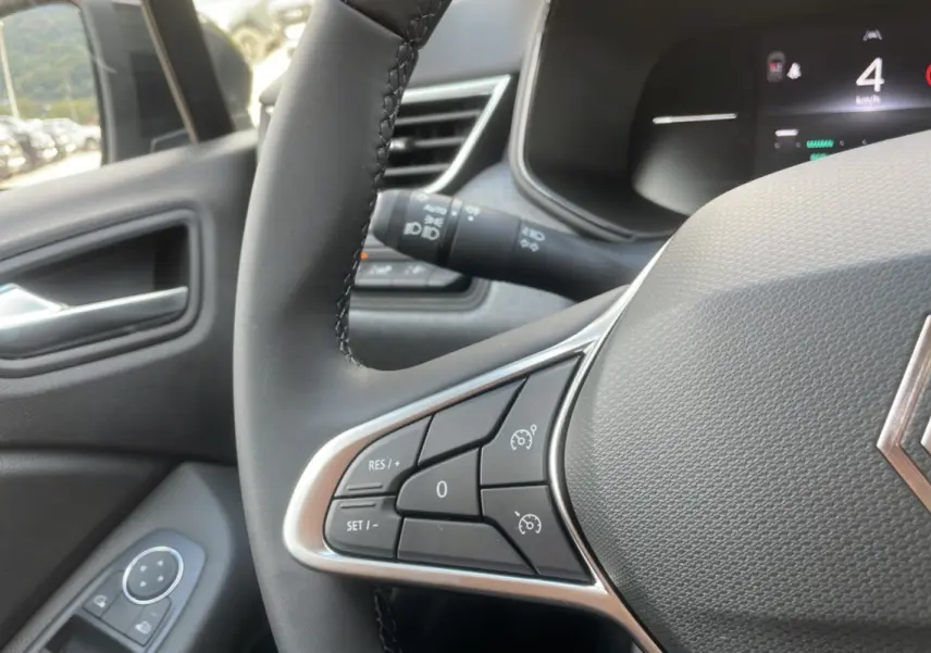 Gros plan sur le volant multifonctions de la Renault Clio 2025, avec commandes de régulateur et tableau de bord numérique.