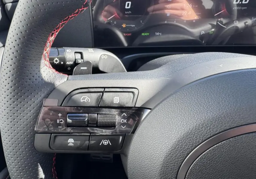 Gros plan sur le volant cuir noir avec surpiqûres rouges du Hyundai Tucson N Line 2025, affichage numérique en arrière-plan.