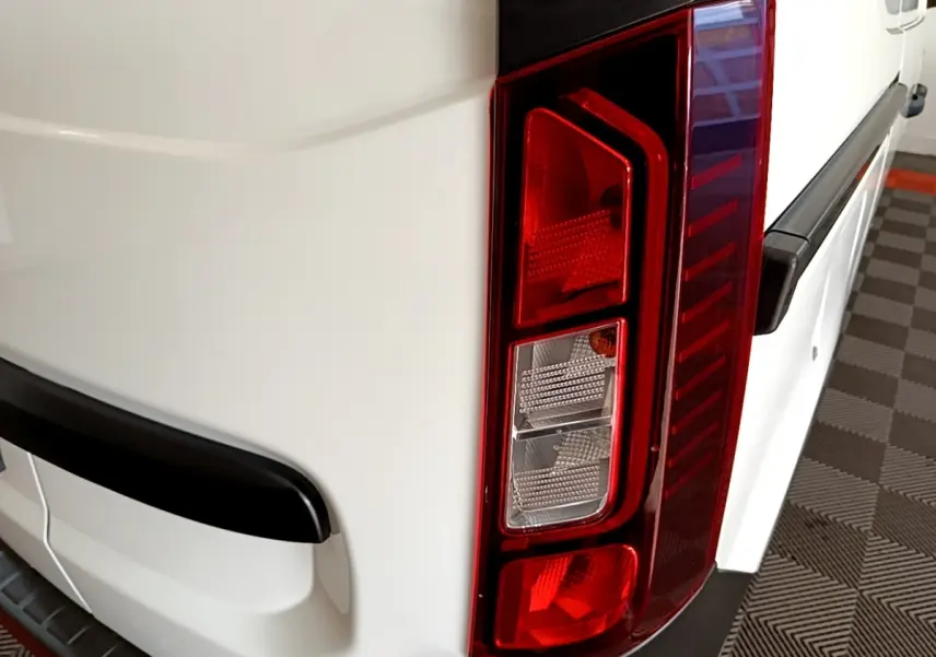 Gros plan sur le feu arrière droit d’un Renault Express blanc, avec pare-chocs noir et surface lisse du véhicule.