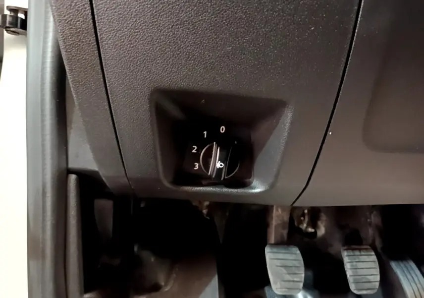 Détail du réglage manuel des phares dans l'habitacle d'un Renault Express blanc, vue côté conducteur vers les pédales.
