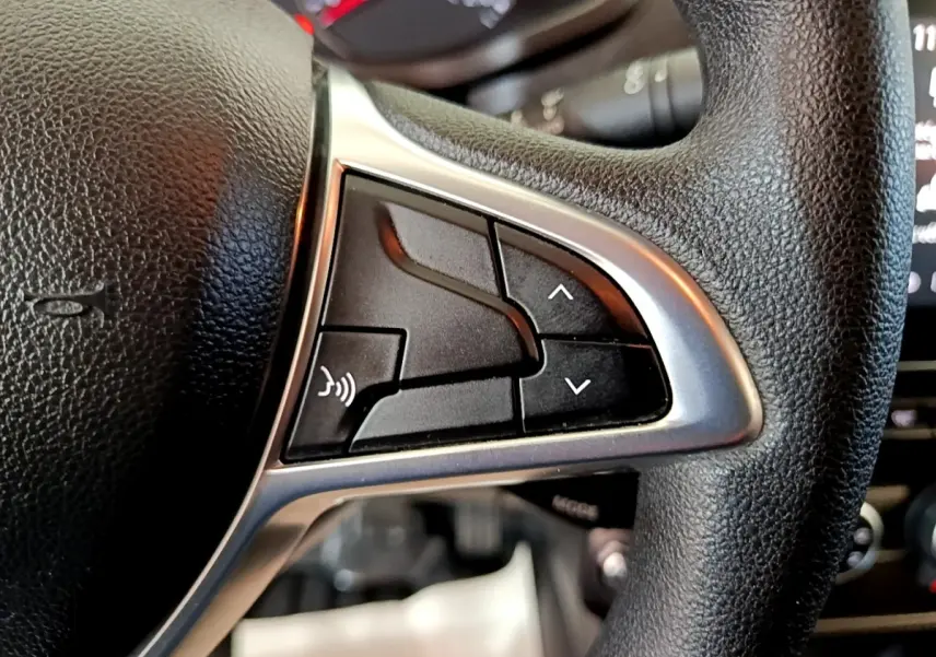 Gros plan sur les commandes gauche du volant noir du Renault Express blanc, boutons de réglage et commande vocale visibles.