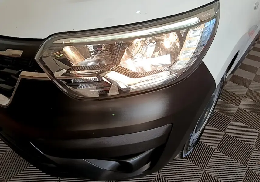 Gros plan sur le phare avant droit allumé d’un Renault Express blanc avec pare-chocs noir mat.