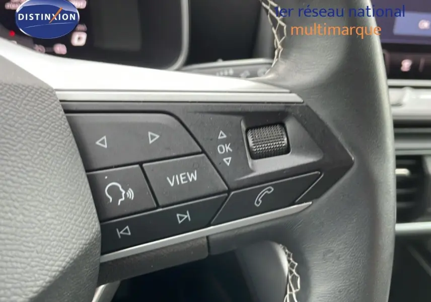Gros plan sur les commandes gauche du volant en cuir noir du SEAT LEON bleu Fjord, avec boutons multifonctions et molette.
