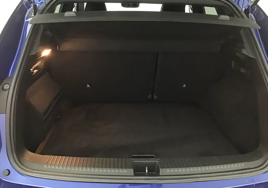 Coffre ouvert vu de l'arrière d'un Renault Austral 2023 bleu iron/noir, montrant l'espace de chargement vide et l'éclairage intérieur.