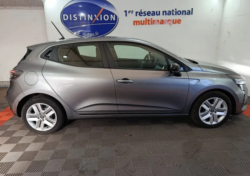 Profil côté gauche d'une Renault Clio gris foncé 2025 Evolution Blue dCi 100 en intérieur avec logo Distinxion en arrière-plan.