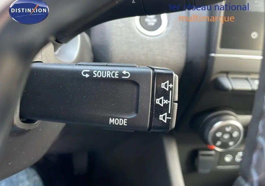 Gros plan sur la commande multifonction noire du volant d’une Renault Clio 2025, intérieur sombre.