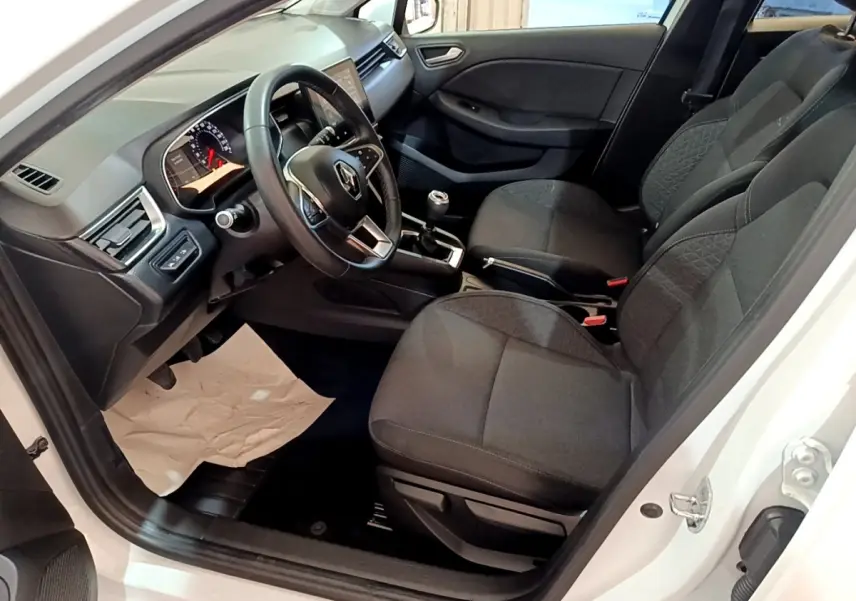 Vue intérieure côté conducteur d'une Renault Clio Business Blue dCi 115 blanche, montrant sièges noirs et volant cuir multifonctions.