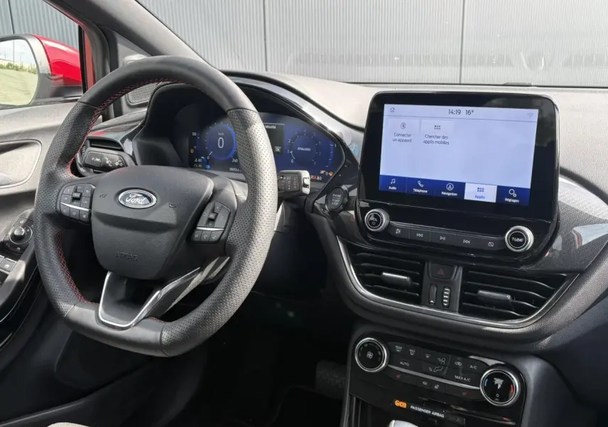 Vue intérieure du tableau de bord et volant ST-Line perforé du Ford Puma rouge avec écran tactile et commandes intégrées.
