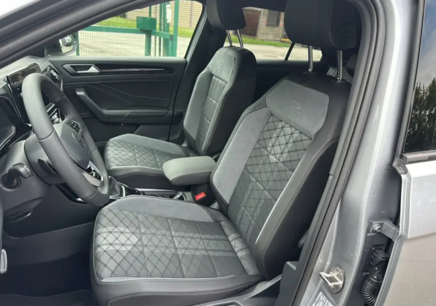 Vue intérieure côté conducteur du Volkswagen T-Roc gris pyrite, mettant en valeur les sièges en tissu avec surpiqûres R-Line.