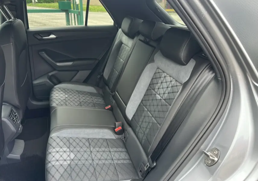 Vue intérieure arrière droite du Volkswagen T-Roc gris pyrite, montrant la banquette arrière en tissu avec motifs géométriques.