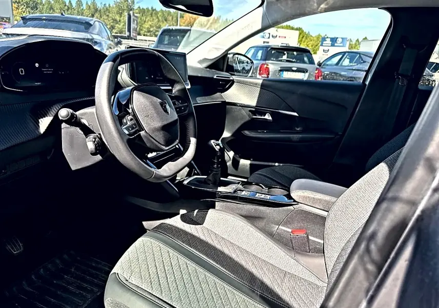 Intérieur de la Peugeot 208 1.2 100 Allure, vue côté conducteur, sièges gris et volant compact avec écran tactile.