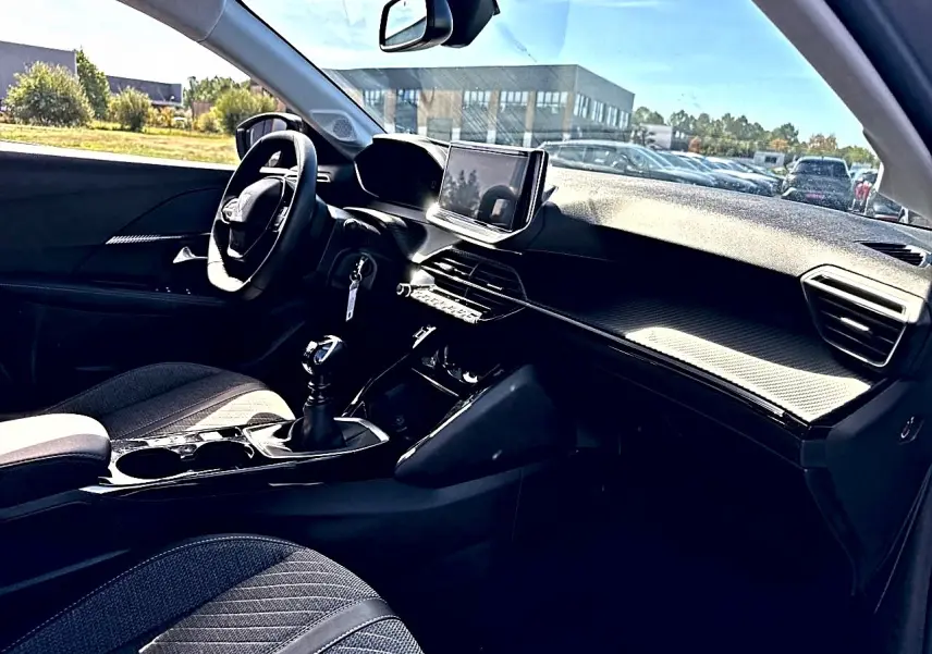 Intérieur de la Peugeot 208 1.2 100 Allure vu côté conducteur, tableau de bord noir avec écran tactile et volant compact.
