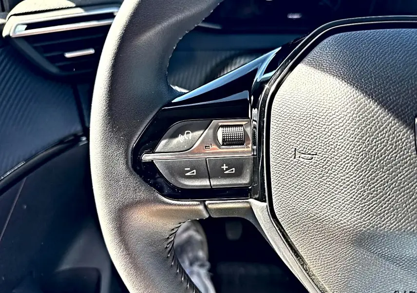 Gros plan sur le volant noir de la Peugeot 208 1.2 100 Allure avec commandes audio intégrées côté gauche.