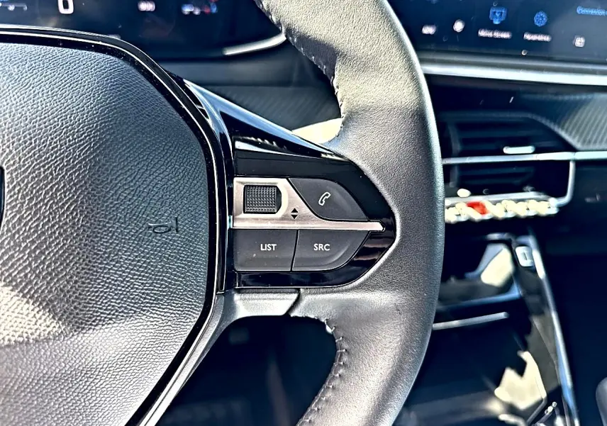 Gros plan sur le volant cuir noir côté gauche du Peugeot 208 1.2 100 Allure avec commandes audio intégrées.