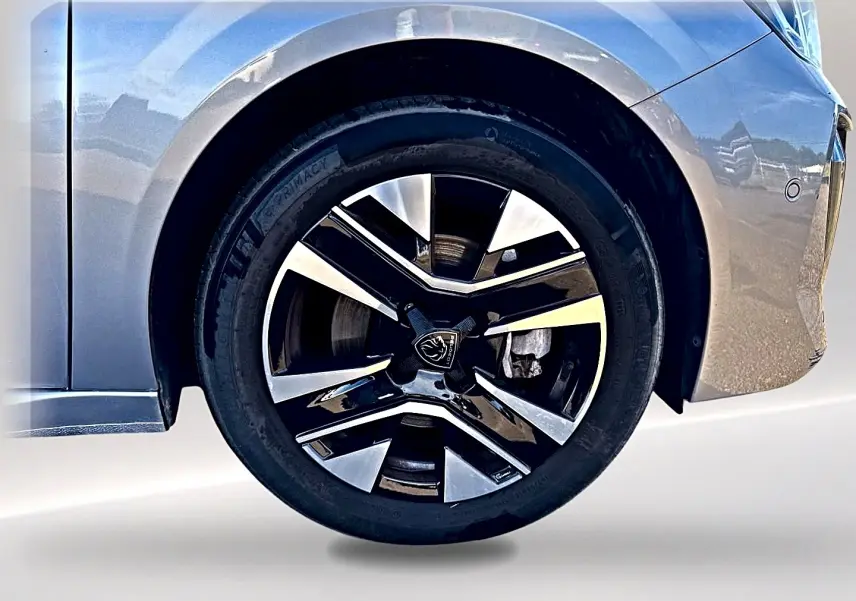 Gros plan sur la roue avant droite gris artense d'une Peugeot 208 1.2 100 allure avec jante alu bicolore.