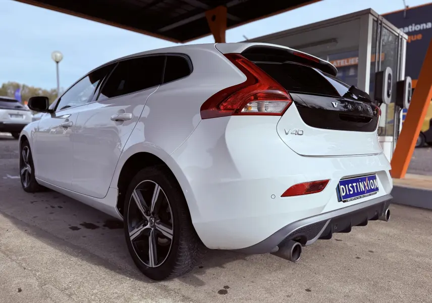 Vue 3/4 arrière droite d'une Volvo V40 blanche R-Design avec jantes noires et feux arrière distinctifs.