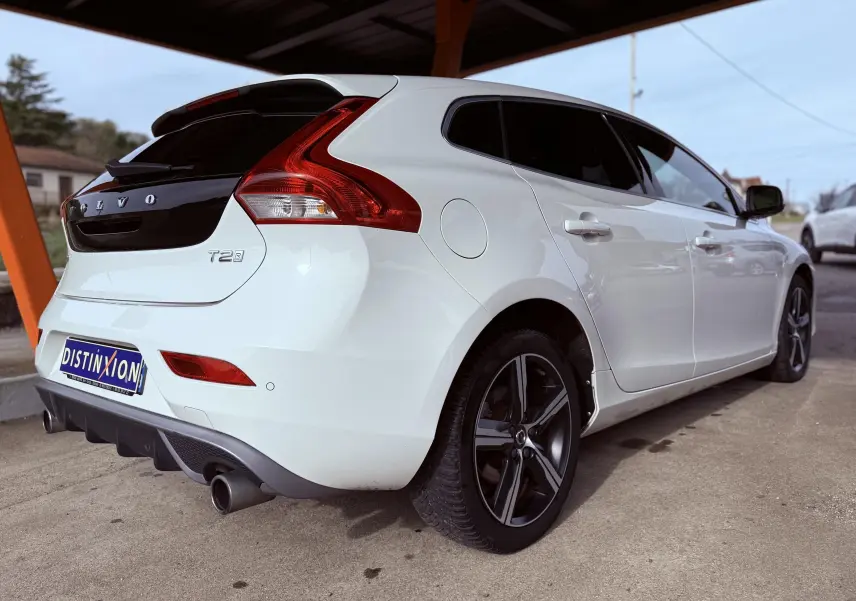 Vue 3/4 arrière droite d'une Volvo V40 R-Design blanche avec jantes sport et feux arrière distinctifs.