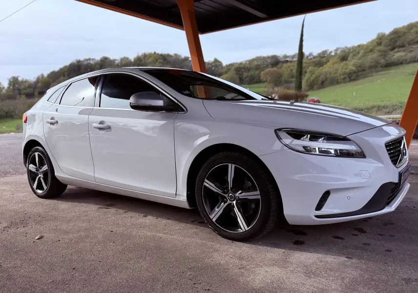 Vue 3/4 avant droite d'une Volvo V40 blanche R-Design 2017 avec jantes alliage noires et vitres teintées.